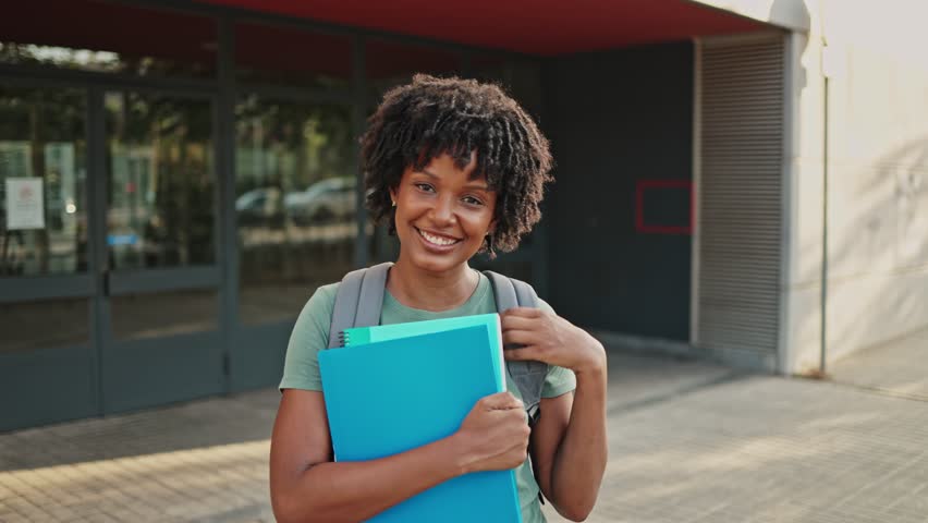 Student smiling holding books slow motion. Young female student smiles while holding books, showcasing joy and confidence in a vibrant, slow-motion moment