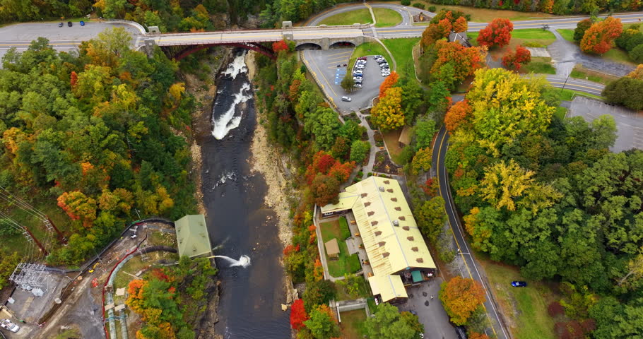 Car goes by the bridge crossing the river flowing in the rocks. Drone footage above the colorful autumn forest in Ausable Chasm in Adirondacks, NY, USA.