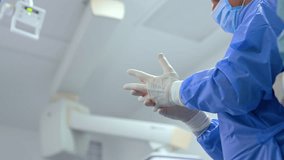 Unrecognized surgeon in blue robe putting on latex gloves. Assistant tying the coat. Low angle view. Preparation for operation. - Powered by Shutterstock - Get 15% off with code: PIKWIZARD15