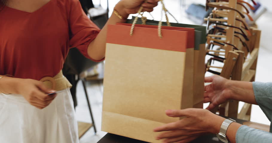Close-up view of payment transaction in fashion boutique store. Female customer extends card to reader NFC terminal to complete purchase. Modern technology usage for contactless payments, consumerism