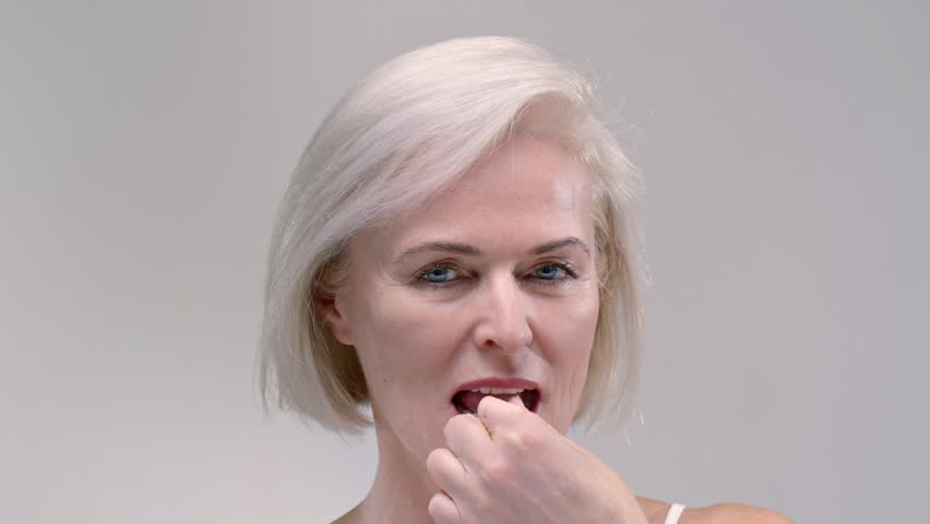 Old woman takes a yellow capsule with fish oil with hand. Senior female eats a pain pill or dietary supplement, taking medicine. Analyzing, Industry Medication. Elderly lady puts the drags in mouth