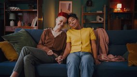 Lesbian couple sits on sofa and relaxes in serene atmosphere. Happy women hold hands tenderly resting on comfortable couch in cozy living room - Powered by Shutterstock - Get 15% off with code: PIKWIZARD15