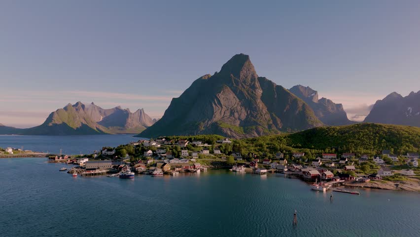 Explore a picturesque coastal village in Norway nestled between majestic mountains and tranquil waters. The sun casts a warm glow, Reine village Lofoten