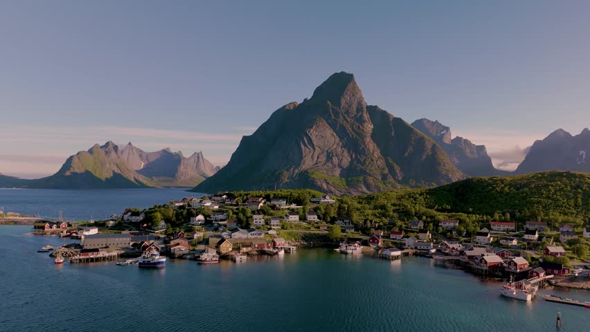 Explore a picturesque coastal village in Norway nestled between majestic mountains and tranquil waters. The sun casts a warm glow, Reine village Lofoten