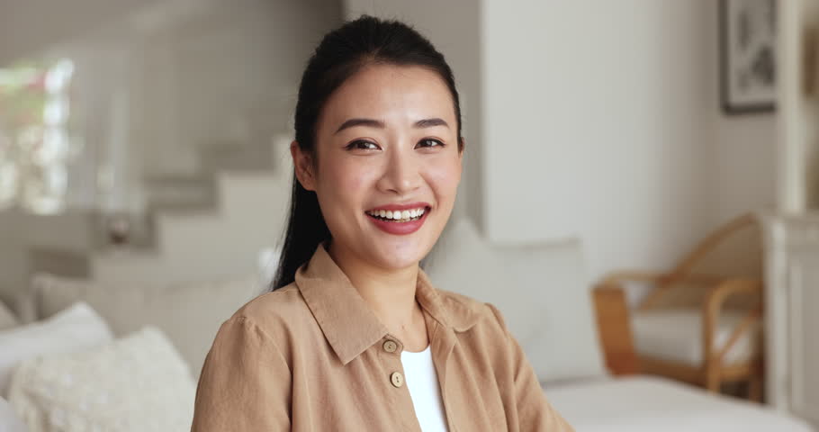 Serious beautiful young Vietnamese woman posing for portrait at home, getting happy, cheerful, smiling, laughing, reacting to good, positive news. Asian female model indoor head shot