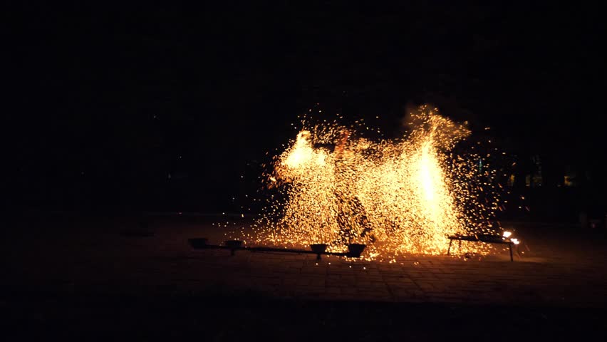 The artist of the fire show in black clothes throws fiery golden sparks. An impressive beautiful performance with fire and fireworks. Slow motion. A professional circus performer dancing with fire.