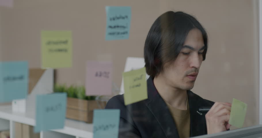 Asian man office employee working with sticky notes writing thinking focused on project at work. Businessman and creative activity concept.