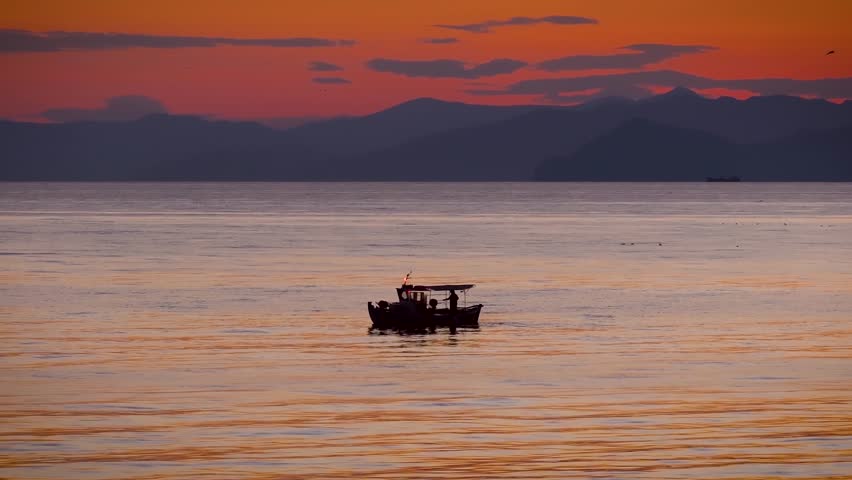 Panoramic aerial view of a fishing boat on calm sea during a colorful sunset in the Aegean Sea, Greece, as a background