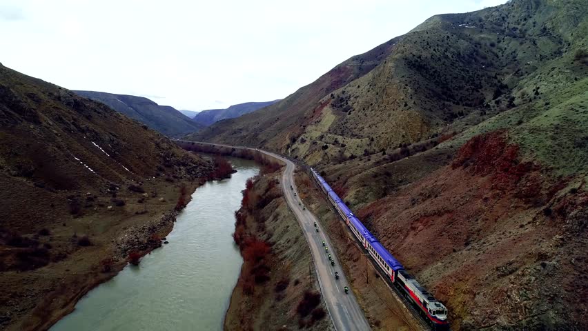 In autumn, a train enters a tunnel as motorcycles ride alongside, their riders cruising in sync. Narrow-gauge trains near the river run on tracks, carrying cargo or passengers.