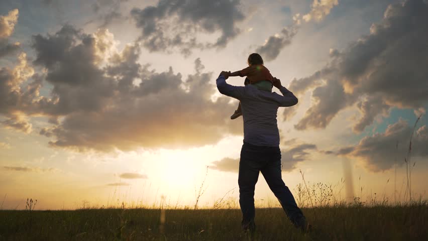 Father with child outdoors at sunset. Happy family moments outdoor. Silhouette of man carrying child in scenic field. Emotional bond between family members. Concept of love, family, and outdoor fun.
