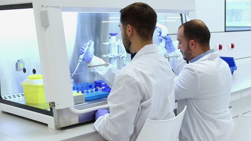 Two professional laboratory scientists in white coats working together in a modern, bright laboratory, conducting experiments and research using advanced equipment to develop new medicines