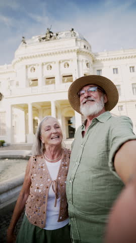 Senior couple taking selfie. Pensioners enjoying hot summer in the city, sightseeing, taking walk in historic part of city. Staycation concept.