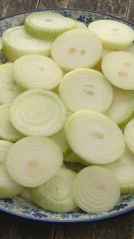 Raw sliced yellow onion on a plate. Table spin. Vertical video.
