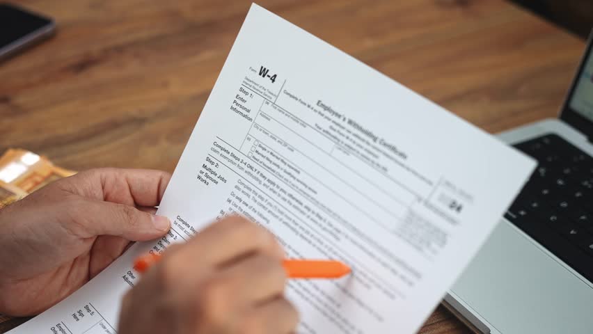 Office worker holds W-4 tax declaration in hands carefully reading paragraphs of document man arranges workplace with euro banknotes and laptop slow motion