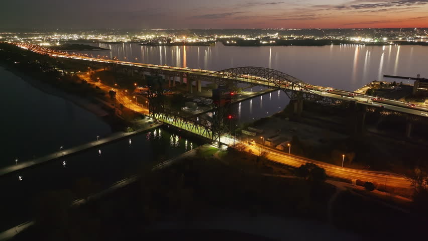 Burlington Skyway Bridge at dusk, urban skyline, calm waters, bridge lights