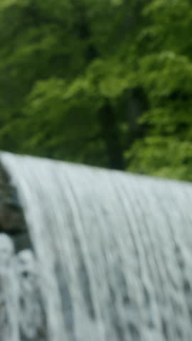 Vertical video. Young man with backpacker looking at the handmade waterfall. Hiker man trekking, enjoying beautiful waterfall.