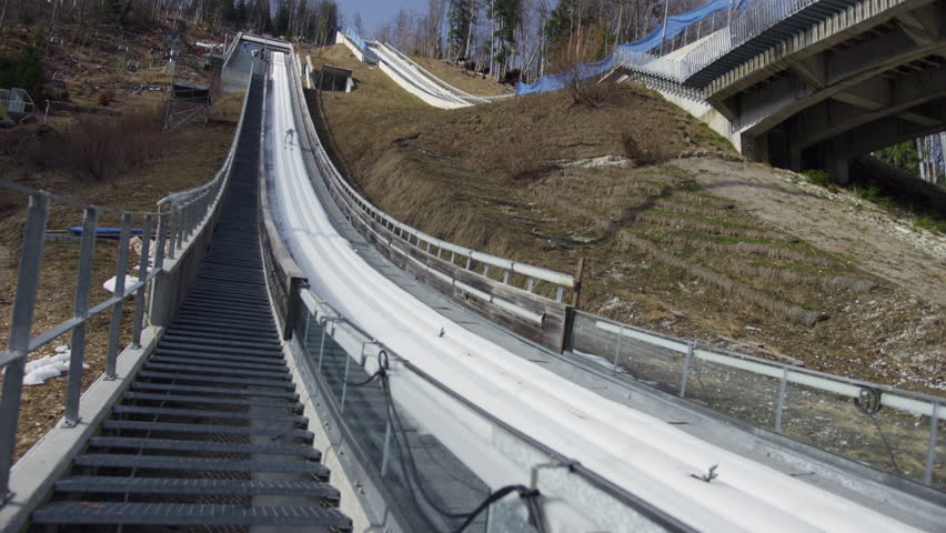 Ski jumper in the inrun, from the top of the ski jump, skiing down in a crouched position, handheld shot. Slovenia and ski sports destination concepts.