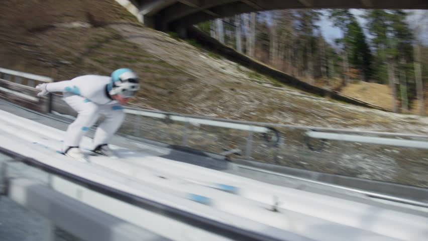 Ski jumper in the inrun, from the top of the ski jump, skiing down in a crouched position, handheld shot. Slovenia and ski sports destination concepts.