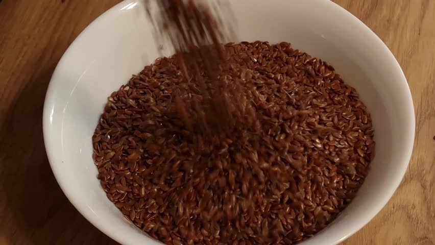 Flax seeds falling into a white bowl. Healthy nutrition, dieting concepts