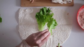 Female hands preparing a wrap with fresh lettuce, tomatoes, sauce and shrimp on a flat tortilla. Part of series - Powered by Shutterstock - Get 15% off with code: PIKWIZARD15