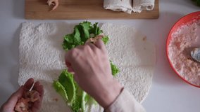 Female hands preparing a wrap with fresh lettuce, tomatoes, sauce and shrimp on a flat tortilla. Part of series - Powered by Shutterstock - Get 15% off with code: PIKWIZARD15