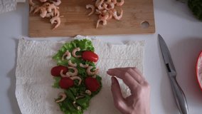 Female hands preparing a wrap with fresh lettuce, tomatoes, sauce and shrimp on a flat tortilla. Part of series - Powered by Shutterstock - Get 15% off with code: PIKWIZARD15