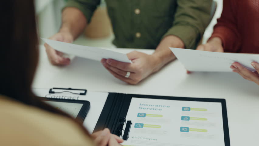 Asian couple examines important documents closely, collaborating on financial and insurance planning in a professional setting with an advisor.