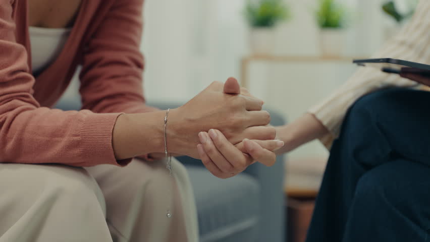 A woman holds hands tightly during a counseling session, symbolizing emotional support, trust, and guidance while discussing relationship struggles with a therapist.