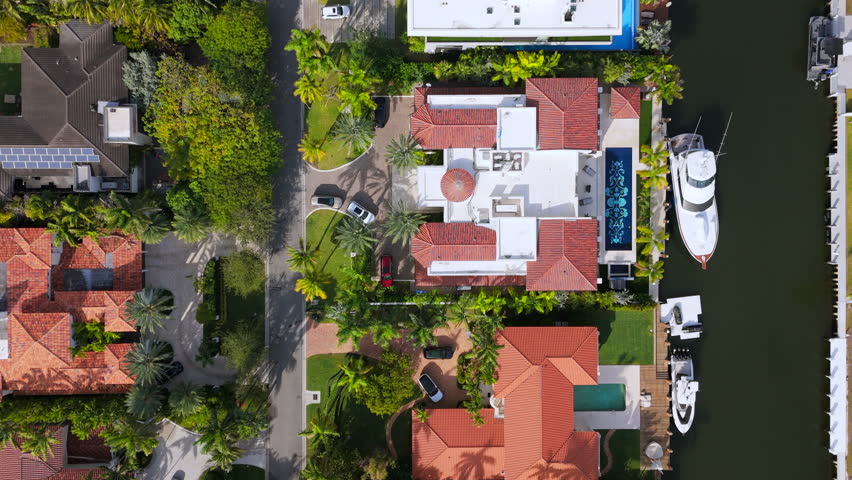 Stunning and sunny aerial top down view of vibrant Miami Beach neighborhood filled with luxurious homes, sparkling pools, tall palm trees, array of boats dotting the coastal landscape, travel Florida