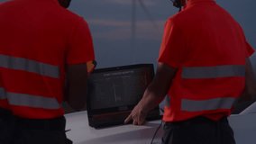 A close-up view of wind turbine data displayed on a laptop features two inspectors analyzing information to ensure system performance and blade rotation efficiency during field operations at dusk. - Powered by Shutterstock - Get 15% off with code: PIKWIZARD15