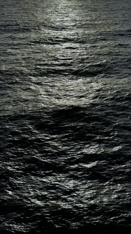 Ocean surface at night with dark blue waters, waves rippling across the vast expanse, creating a mysterious and eerie atmosphere under a silent and remote horizon that stretches into the unknown