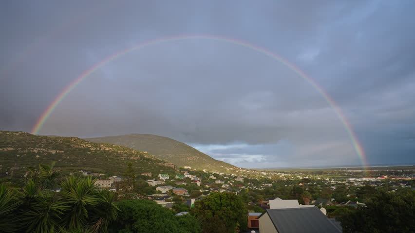 A rainbow shines over mountainous horizon in a surburban setting