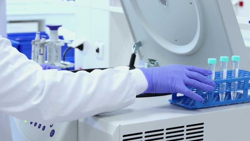 Laboratory technician wearing a lab coat and gloves carefully places samples into a centrifuge for analysis, preparing for scientific experiments - Powered by Shutterstock - Get 15% off with code: PIKWIZARD15