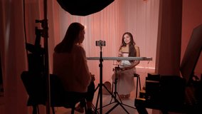 Backstage shooting woman model in dress sitting and talking, female assistant recording podcast on smartphone in studio with pink fabrics background. Beauty blogger concept. - Powered by Shutterstock - Get 15% off with code: PIKWIZARD15