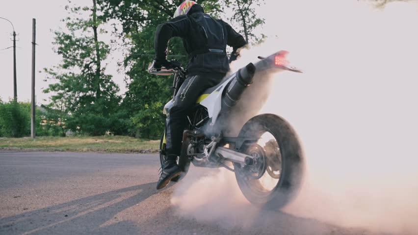 Motorcyclist doing tire burnout. Slow motion, the wheel rotates in place in the rays of the setting sun.