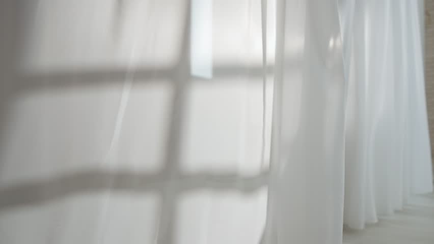 Transparent white silk soft fabrics floating from an open window with light shining through, window door silhouette reflected on textile.