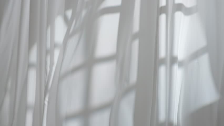 Transparent white silk soft fabrics floating from an open window with light shine through, shadows reflected on the textile, full shot.