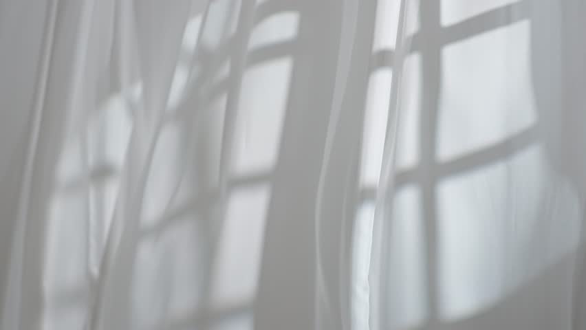 Transparent white silk soft fabrics floating from an open window with light shine through, shadows reflected on the textile, full shot.