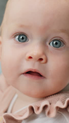 Vertical close up portrait of cute baby girl with blue eyes looking at camera