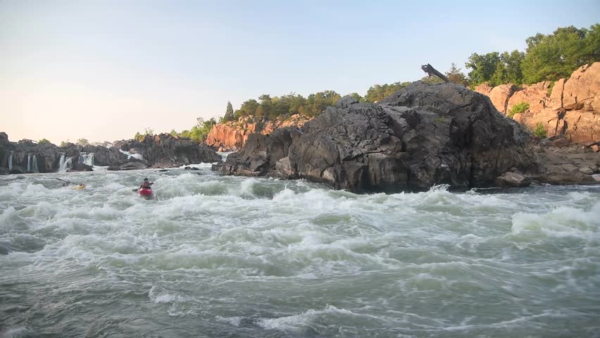 Two men kayaking on a river with rocky banks down a mountainous rough water at sunset.