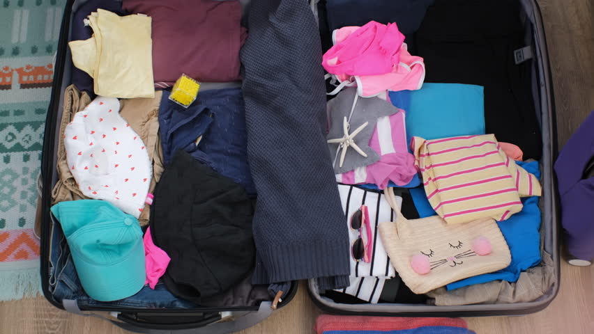 Mother and daughter pack a suitcase with swimsuits, flippers, and summer clothing, eagerly anticipating their upcoming vacation together. Organizing luggage, slow motion. View from above