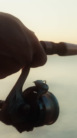 Vertical video. Man with a fishing rod stands on the shore fishing on the sea and enjoying nature aganist of sunset