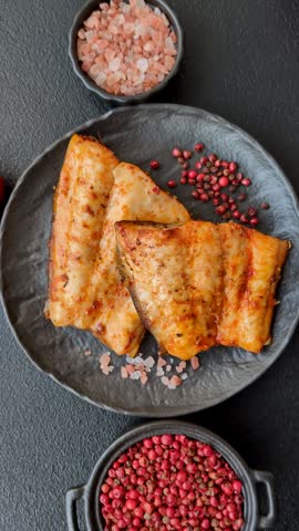 Grilled fish fillet with salt, spices and herbs on dark concrete background