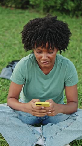 Young woman relaxing on grass using smartphone. Young student relaxing on the grass, using a smartphone and enjoying a sunny day outdoors. Happy and carefree moments captured