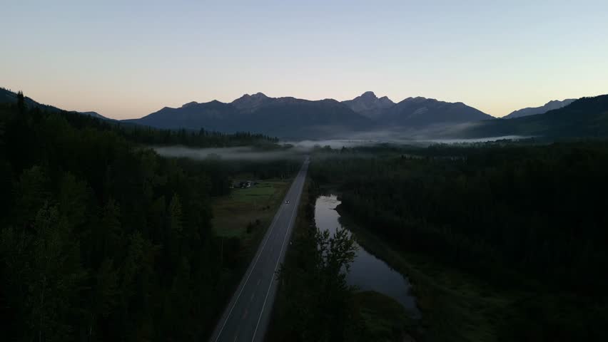 Beautiful aerial drone footage of a highway stretching through a mountain valley shrouded in morning fog. British Columbia, Canada.