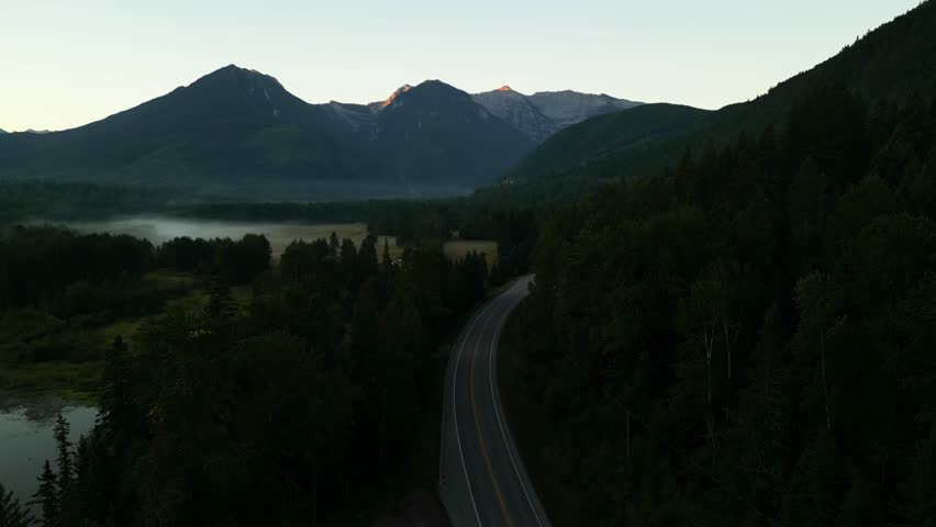 Aerial view of cars driving towards the mountains on a winding country road in the early morning. British Columbia, Canada.