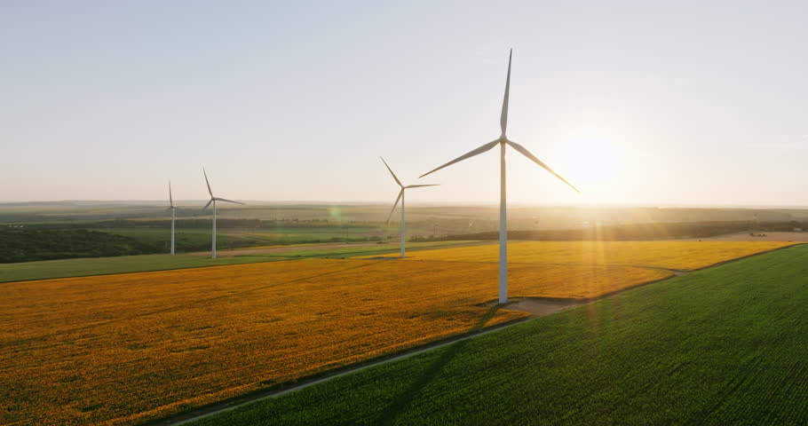 Wind turbines with blades in field aerial view bright orange sunset blue sky wind park slow motion drone turn. Silhouettes windmills, large orange sun disc summer lens flare. Alternative energy