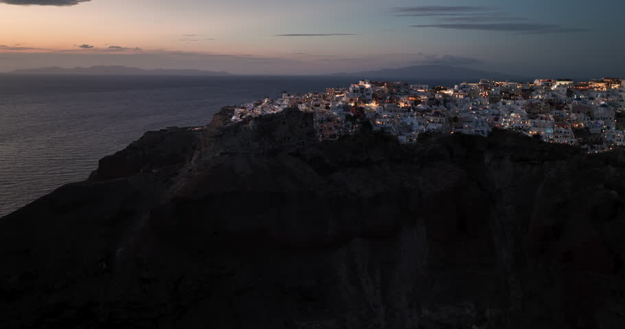 Aerial high angle view of sunset over beautiful town of Oia on the Santorini Island, Greece. Illuminated white buildings on the cliff	