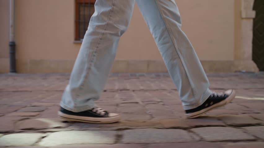Woman walking on road, close up. Side view of female legs wearing sneakers walk on cobblestone street. Tourist in shoes walks on city street