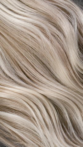 Vertical blond hair texture, slow motion of female hand combing long curly hair